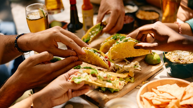 Multiple Hands Holding Tacos Over a Shared Table