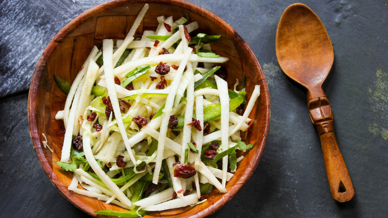 Wooden bowl of jícama slaw next to wooden spoon.