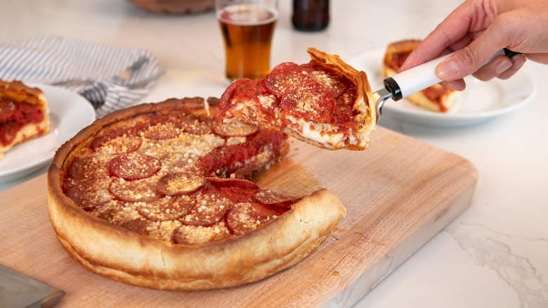 a triple pepperoni deep dish pizza from Giordano's served on a wooden board with a person lifting one slice with a spatula