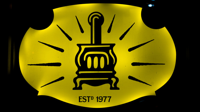 an illuminated yellow Potbelly's logo with an old fashioned stove, a burst design, and established 1977 written across the bottom