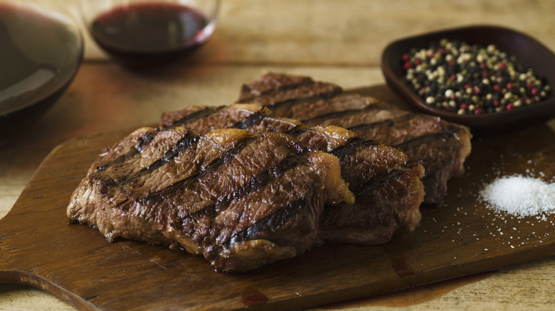 Slice of steak on a table next to a glass of red liquid