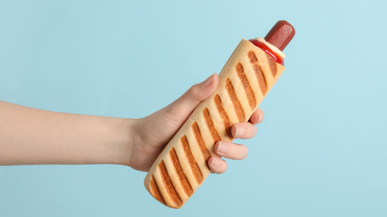 Hand holding hot dog stuffed French baguette