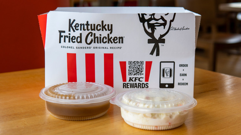Side view of open KFC box and containers of coleslaw, mashed potatoes, and gravy on a restaurant table
