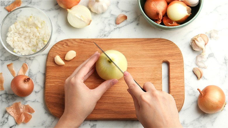 Knife cutting into yellow onion 
