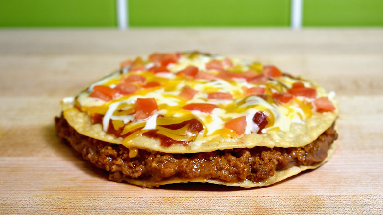 Taco Bell's Mexican pizza on a table with a green wall in the back