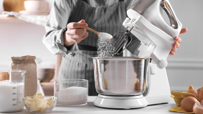 Someone putting sugar into a mixing bowl