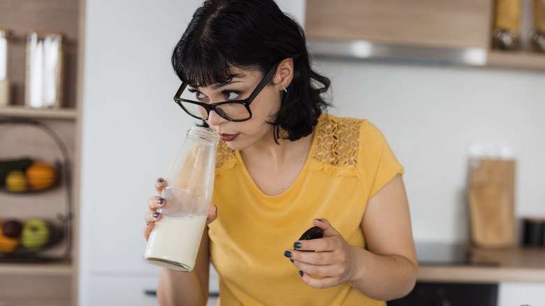 Woman smelling opened milk container before adding it to cereal
