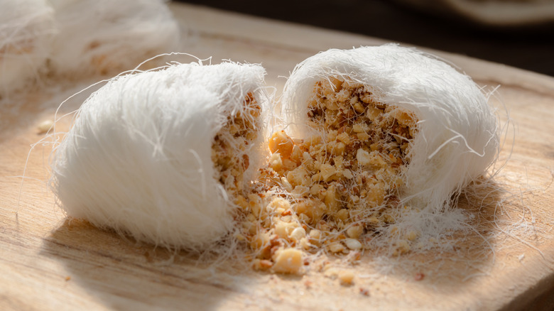 Dragon's Beard candy cross section spilling with nuts, coconut and sesame seeds on a wooden board