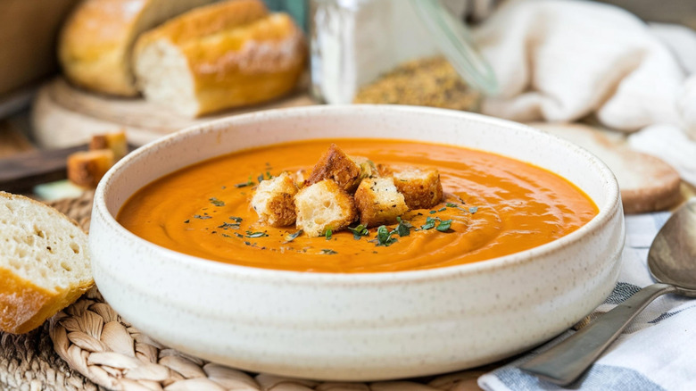 Brownish soup with croutons, leafy garnish, and bread in background