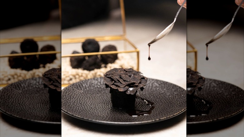 Spoon drizzling sauce over black truffle dish
