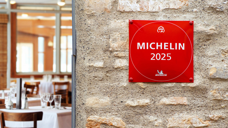 A 2025 Michelin star sign on a stone wall with a restaurant dining room in the background