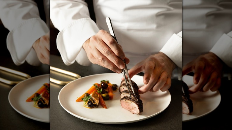 Chef plating meat with silver tnogs