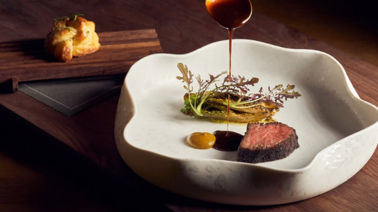 Spoon drizzling sauce on a steak that sits on a white plate