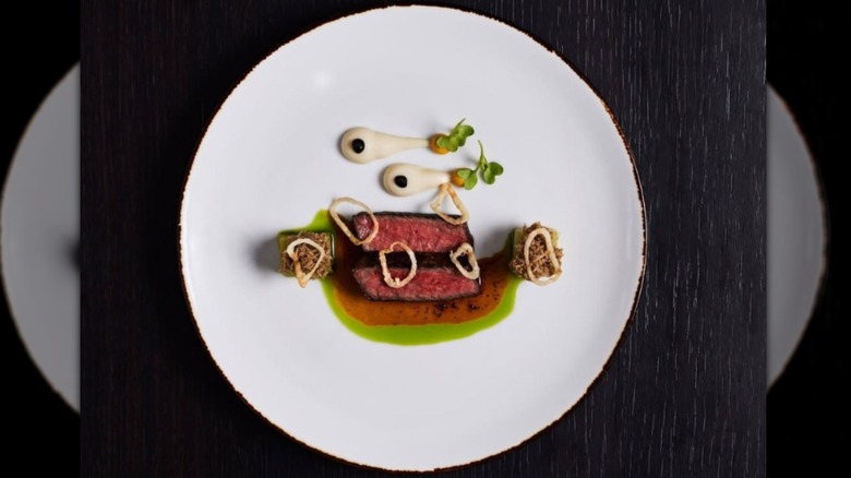 A white plate with steak and drizzles of green and red sauces