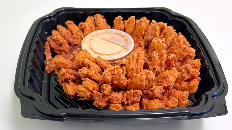A cactus blossom and dipping sauce in a black container against a white background