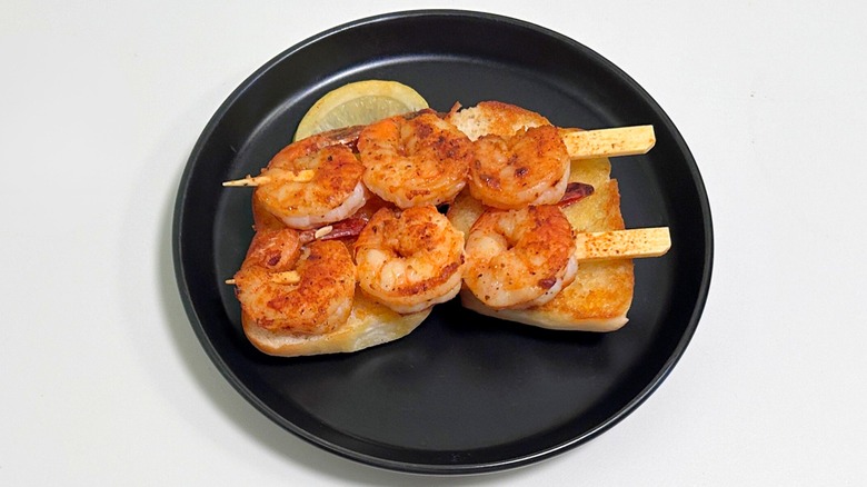 Grilled shrimp kabobs and toasted bread on a black plate against a white background
