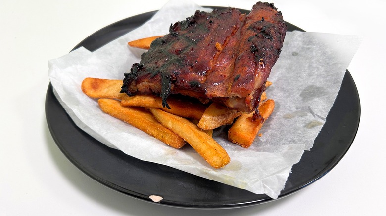 Barbecue ribs and fries on a black plate against a white background