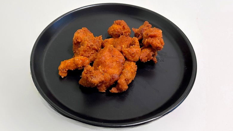 A plate of boneless buffalo wings on a black plate against a whitish gray background