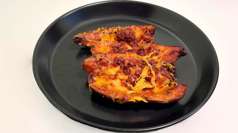 A plate of potato skins with cheese and bacon on a black plate against a white background