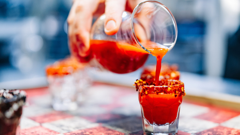 Man's hand pouring sangrita into shot glass