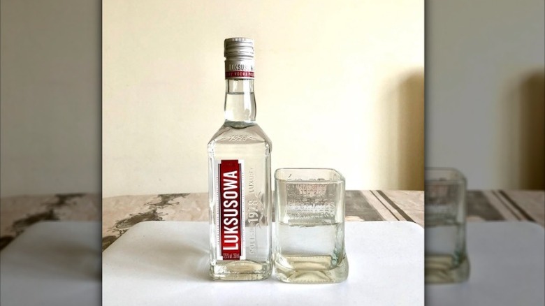 A close up of a bottle of Luksusowa vodka next to a clear glass with vodka in it