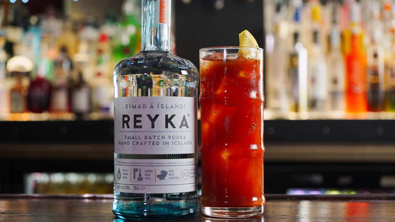 A close up fo a Reyka vodka bottle next to a bloody mary cocktail