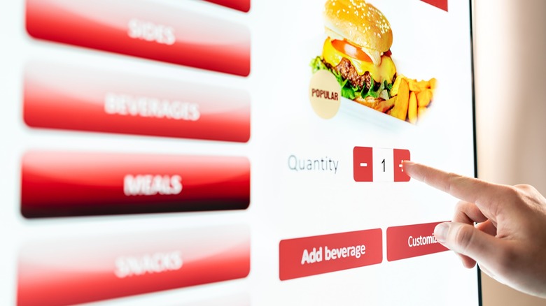 Person touching a touchscreen ordering a burger and fries
