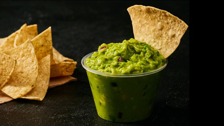 Side order of Chipotle guacamole in small plastic container surrounded by tortilla chips