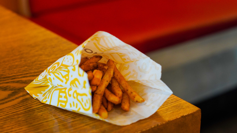 Fast food fries in a paper bag on a wooden table