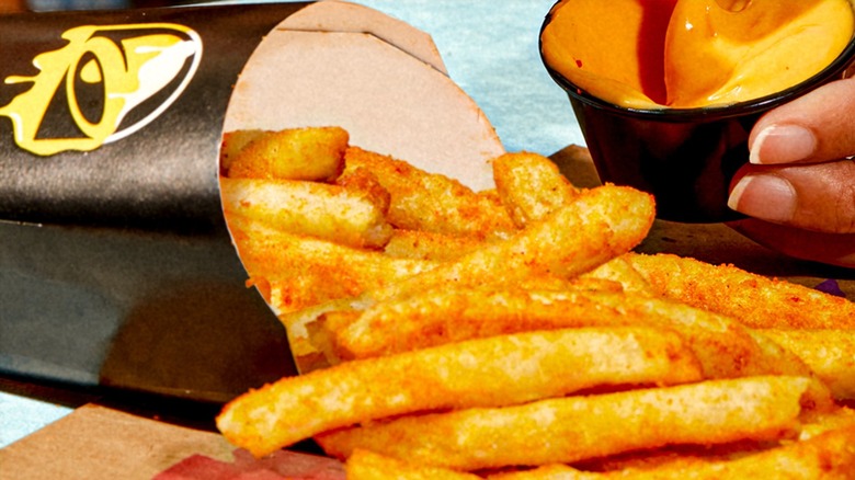 Container of Taco Bell nacho fries with a side of queso dipping sauce
