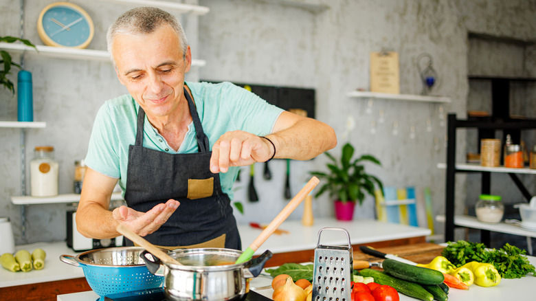 Person adding salt to soup during cooking
