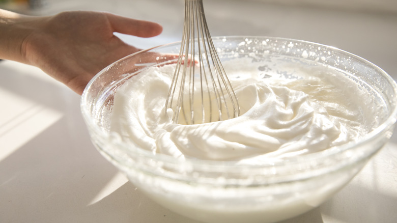 Hand whisking whipped cream in a glass bowl