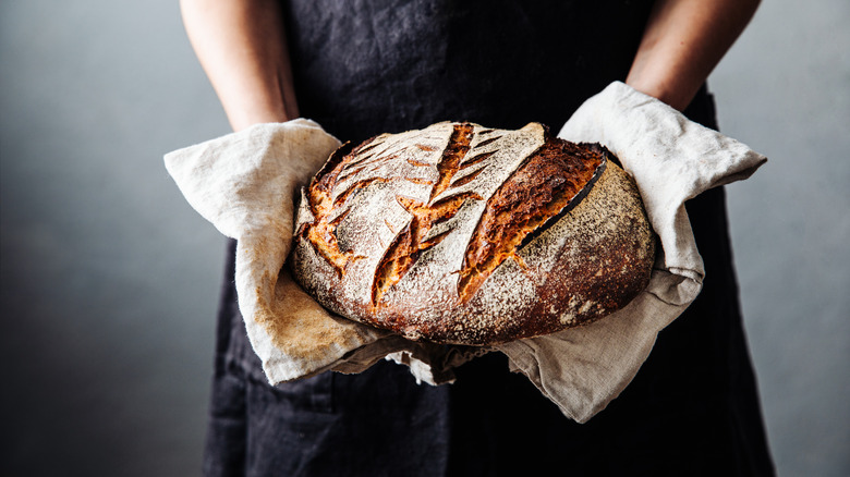 a person holding a sourdough loaf with towels