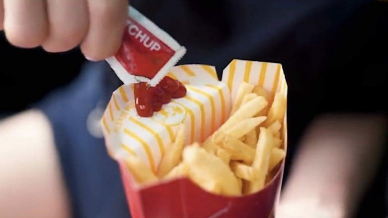 Hand squeezes ketchup packet onto carton flap of McDonald's fries