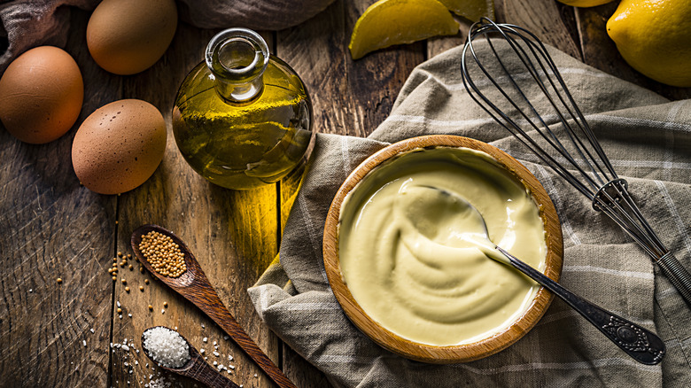 Eggs with jar of oil, whisk, and bowl of mayonnaise