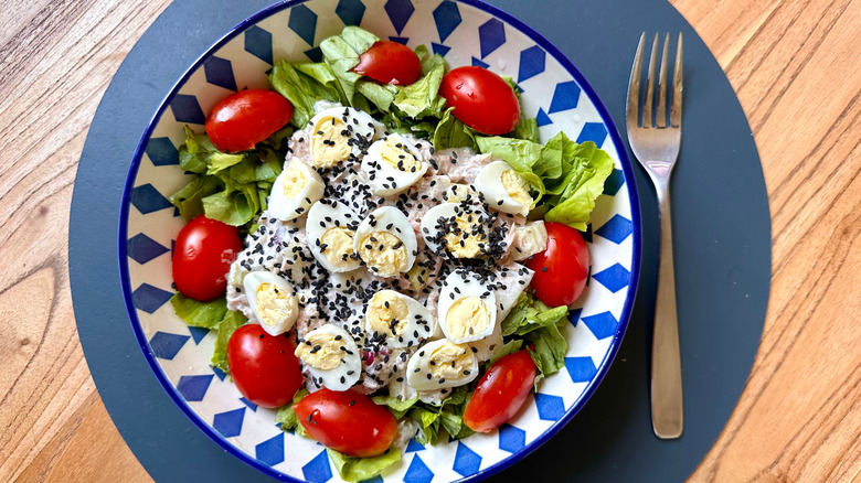 Bowl of tuna salad made with Greek yogurt, hard boiled eggs, leafy greens, and tomatoes