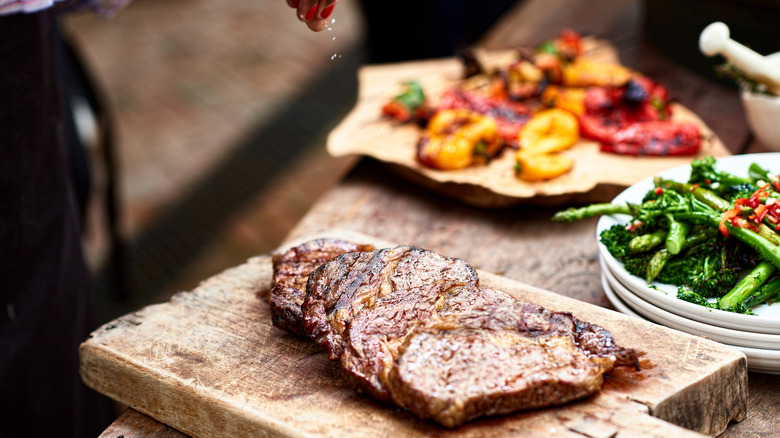 Person salting seared steak on cutting board