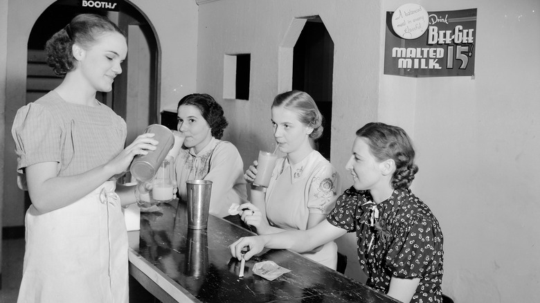 Woman pours drink into glass at soda parlor 