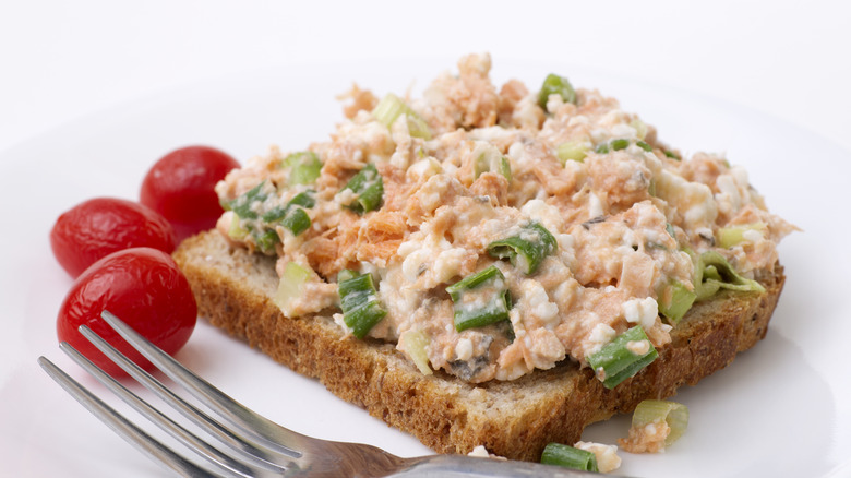Open-faced salmon salad sandwich with green onions and tomatoes on the side.