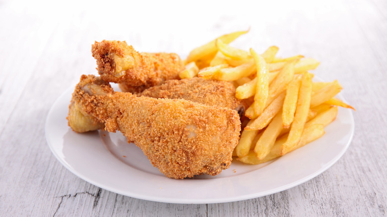 Fried chicken legs with fries on white plate