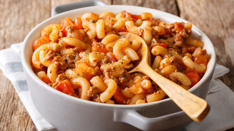 A pot full of American goulash on a wooden table with a wooden spoon