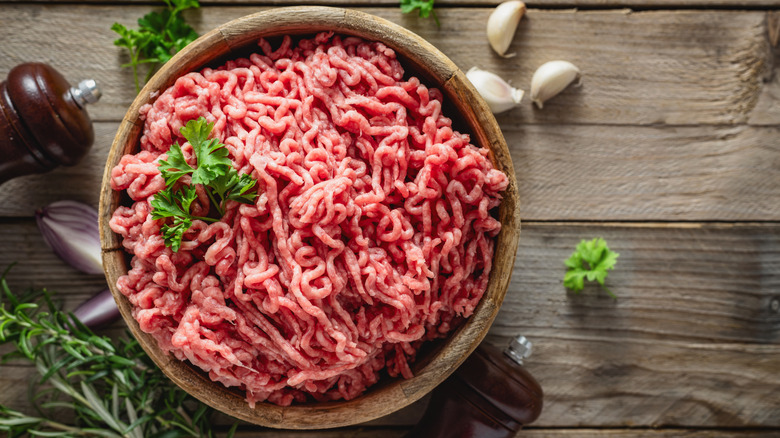 Raw ground beef in a wooden bowl placed on a wooden table
