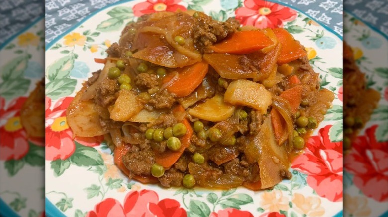 A plate full of shipwreck casserole with ground beef, carrots, peas, and potato slices