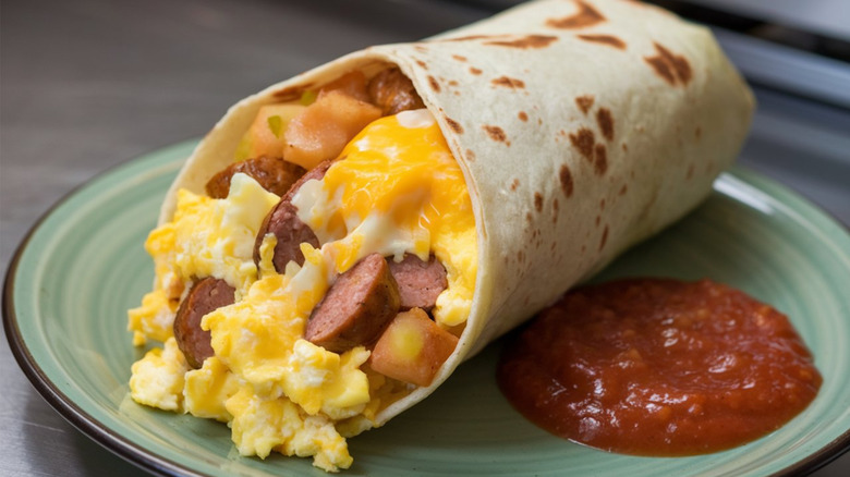 An open ended breakfast burrito on plate with salsa