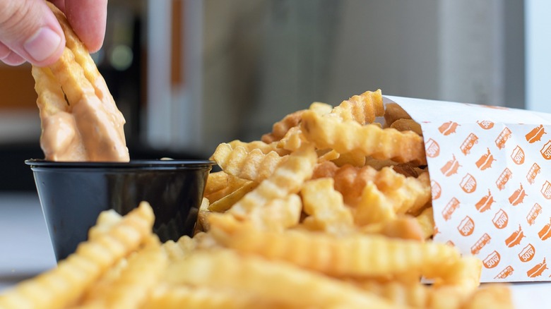 hand dipping fries in sauce