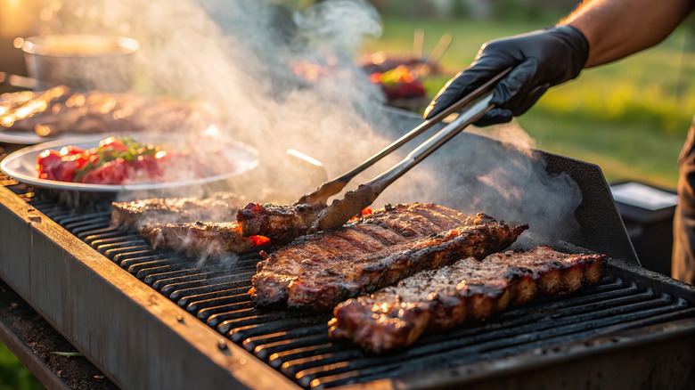 Person using tongs to flip over meats on an outdoor grill