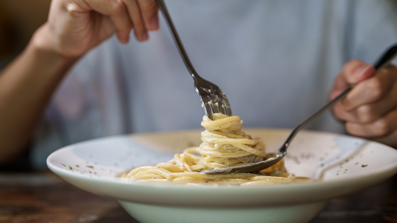 Person twirling alfredo pasta on fork