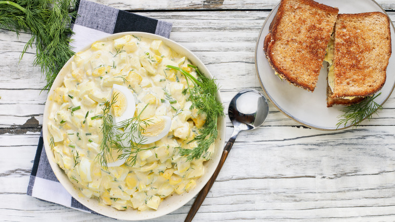 Bowl of egg salad and a side plate of an egg salad on toast with dill garnish