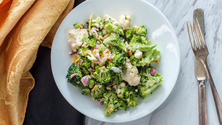 broccoli salad served on white plate next to fork and knife
