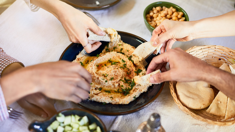 Hands dipping pita into hummus